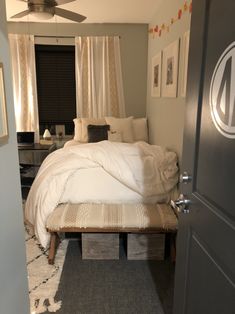 a bed sitting next to a window in a bedroom under a ceiling fan with white curtains