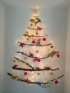 a christmas tree with lights and ornaments in the shape of birds on branches is displayed against a white wall