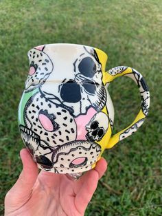 a hand holding up a ceramic mug with designs on it's side in the grass