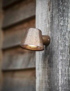 an old fashioned wall light on the side of a wooden building with peeling paint and rusted metal