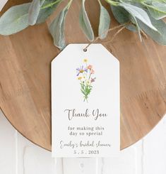 a thank you tag hanging from a wooden plaque with flowers and leaves on the front