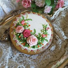 a decorated cake sitting on top of a doily next to pink flowers and lace