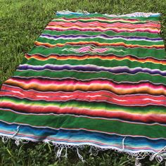 a multicolored blanket laying in the grass on top of some green grass with fringes