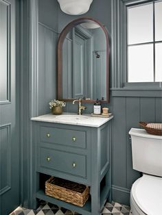 a white toilet sitting next to a bathroom sink under a mirror and a light fixture