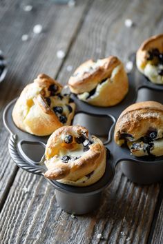 several muffins with blueberries and cream cheese in a muffin tin on a wooden table