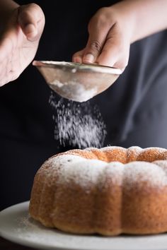 someone is sprinkling sugar on a bundt cake