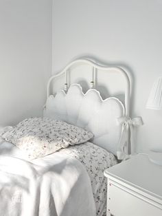 a white bed sitting in a bedroom next to a night stand and lamp on top of a dresser