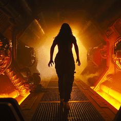 a woman walking through a tunnel in a sci - fi environment with yellow light coming from the ceiling