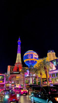 cars are driving down the street in front of some buildings and neon lights at night