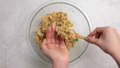 two hands holding a wooden spoon over a glass bowl filled with chopped up food items