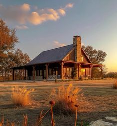 a house in the middle of a field with tall grass and trees around it at sunset