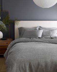 a bed with grey linens and pillows in a bedroom next to a white lamp