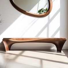 a wooden bench sitting in front of a round mirror on the wall next to a potted plant