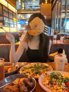 a woman sitting at a table with plates of food in front of her and a donut over her head