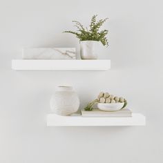 two white shelves with vases and bowls on them, one is filled with flowers