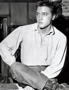 a black and white photo of a man sitting on top of a desk with his hands in his pockets