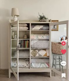 a white cabinet filled with lots of pillows and blankets next to a wall mounted mirror