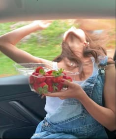 a woman sitting in the back seat of a car holding a bowl of strawberries