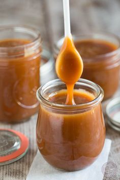 a spoon full of caramel sauce being drizzled over the top of jars