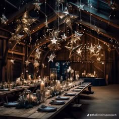 a long table with candles and stars hanging from it's ceiling in a barn