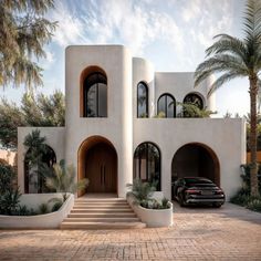 a black car parked in front of a white building with arched windows and palm trees