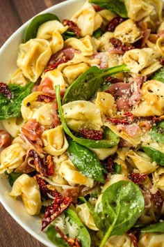 a white bowl filled with pasta salad on top of a wooden table next to a fork