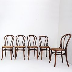 four wooden chairs sitting side by side against a white wall