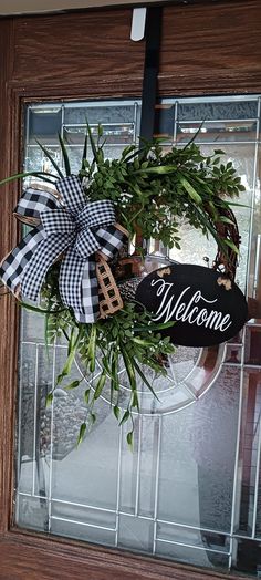 a welcome sign hanging on the front door with greenery and ribbon attached to it