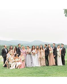 a large group of people in formal wear posing for a photo on the grass with mountains in the background