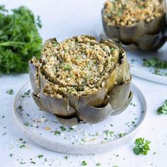 two artichokes on a plate with parsley sprinkled over them