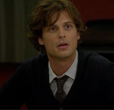 the young man is wearing a sweater and tie in front of his face while looking at something