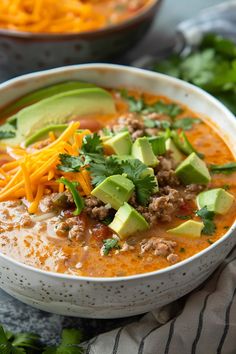 a white bowl filled with soup and topped with cheese, avocado and cilantro