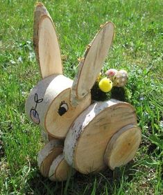 a wooden bunny sitting in the grass with some flowers on it's back end