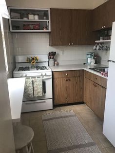 a kitchen with white appliances and wooden cabinets in the corner, along with a rug on the floor