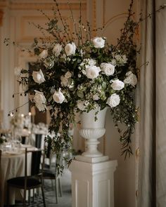 a vase filled with white flowers sitting on top of a table next to a wall