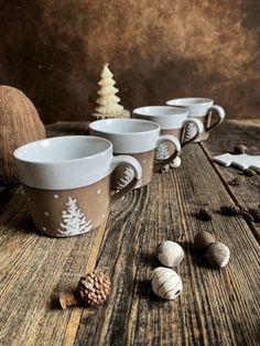 four coffee mugs sitting on top of a wooden table next to small pine cones