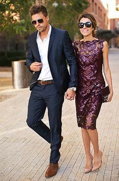 a man and woman are walking down the street holding hands while dressed in formal attire