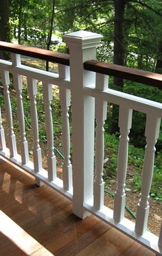 a wooden deck with white railing and wood handrails in front of wooded area