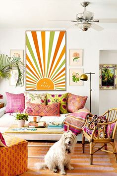 a white dog sitting in front of a colorful couch and chair with art on the wall behind it