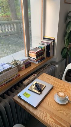 a wooden table topped with a cup of coffee next to a window filled with books