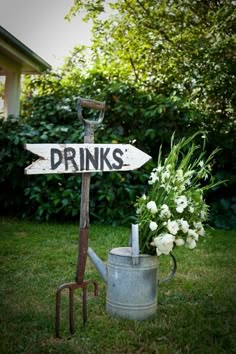 there is a sign that says drink with us on it and a watering can in the grass