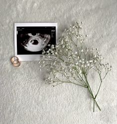 a ring sitting on top of a white flower next to a polaroid print with an image of a woman's face