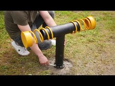 a man kneeling down next to a black pipe with yellow springs on it's ends