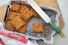 a tray filled with granola bars next to a knife and napkin on top of a cutting board