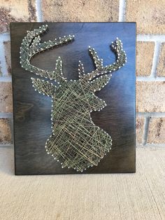 a string art deer head mounted on a wooden plaque with silver beaded antlers