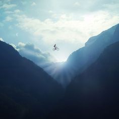 a person on a bike in the air over mountains and valleys with sun shining through clouds