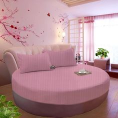 a round bed with pink sheets and pillows in a room decorated with cherry blossom wallpaper