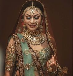 a woman in a green and gold bridal outfit with jewelry on her head, holding a