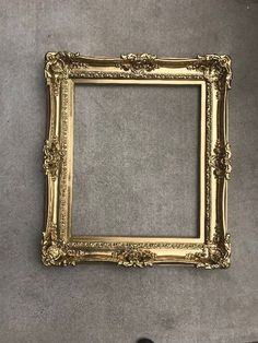 an empty gold frame hanging on the wall next to a pair of shoes and a vase