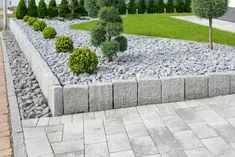 a stone garden bed with trees and bushes in the center, along side a brick walkway